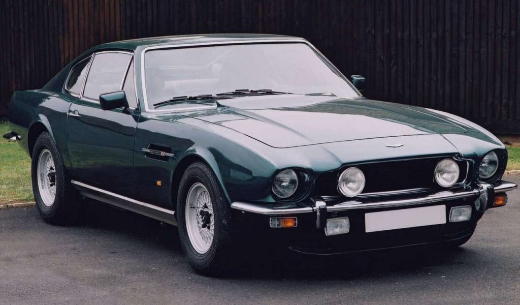 Green Aston Martin parked in front of a fence